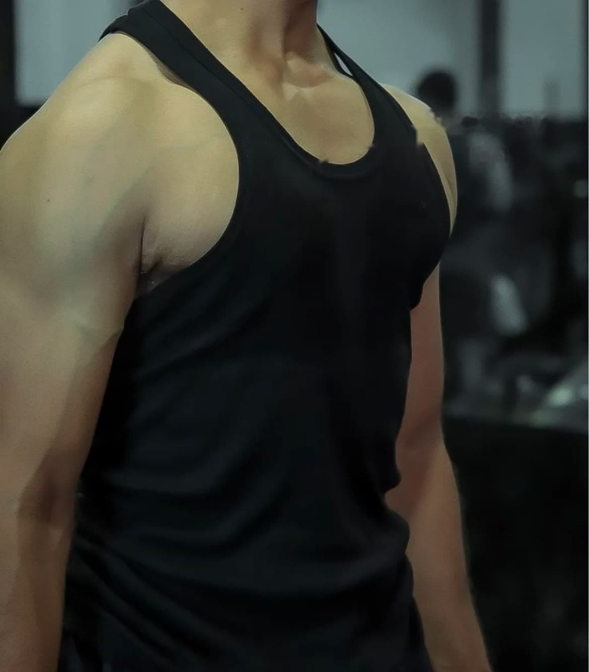 Gymcell black tank top worn in the gym, shoulders and chest in soft light.